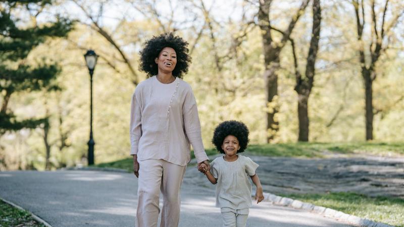 A mother and her young son walk toward us down a tree-lined path, smiling