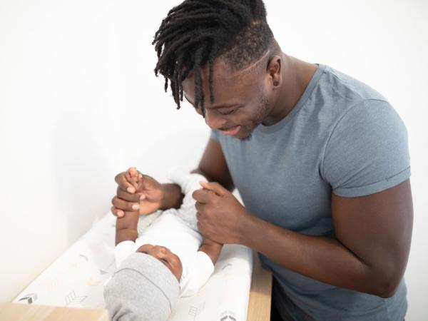 A smiling father plays with his baby on a changing table