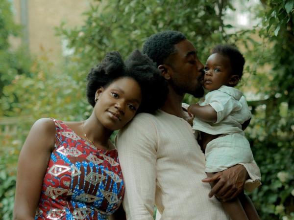 A young couple in a garden, the mother in kitenge print, father holding their baby