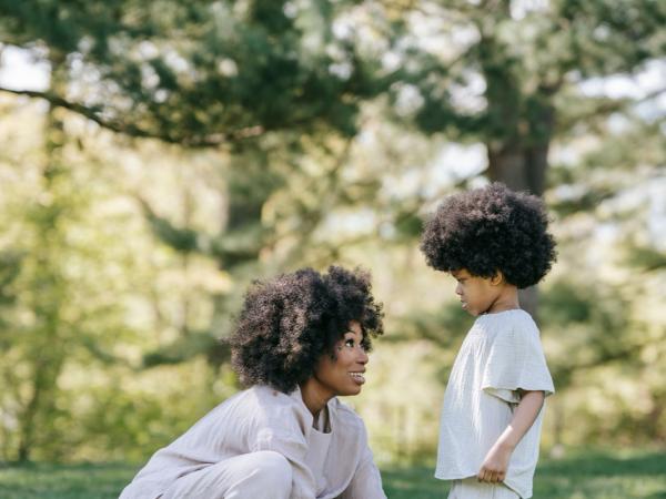 A mother kneels in the grass to tie her young son's shoe