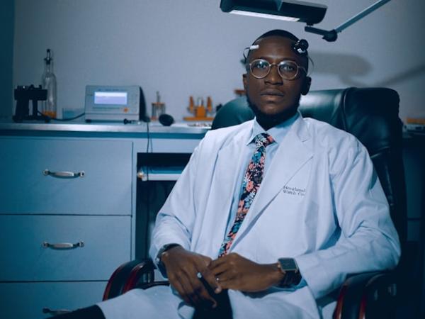 A doctor in a white coat seated in a consulting room.